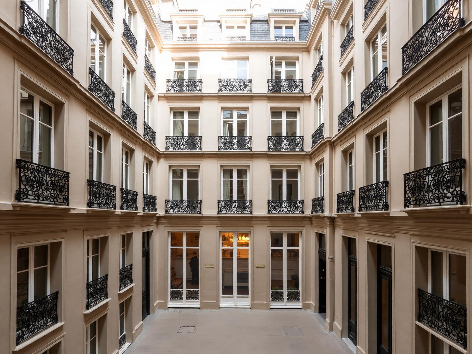 Cour intérieure d'un immeuble haussmannien parisien, façade en pierre de taille et balcons en fer forgé.